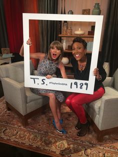 two women sitting in chairs holding up a framed photo with the same person on it