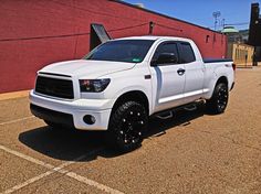 a white truck parked in a parking lot next to a red brick building with black rims