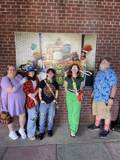 four people standing in front of a brick wall with the muppets on it