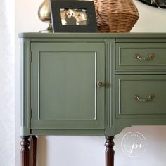 a green cabinet with two pictures on top and a basket sitting on top of it