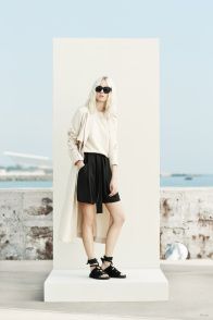 a woman standing on top of a white platform wearing black shorts and a trench coat