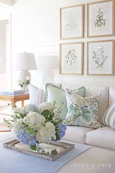 a living room filled with lots of white furniture and flowers on top of a coffee table