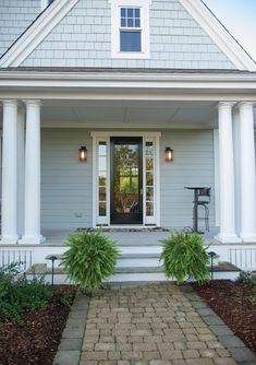 a white house with columns and two plants on the front porch, along with a brick walkway