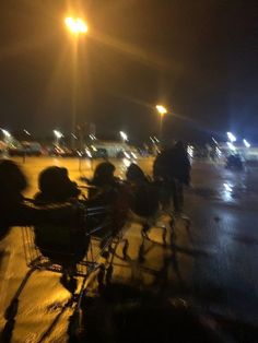 people sitting in chairs on the sidewalk at night with their backs turned to the camera