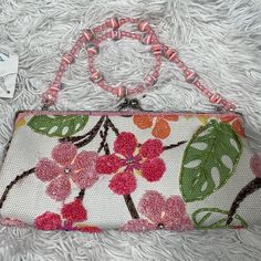 a white purse with pink flowers and green leaves on the front is laying on a furnishing