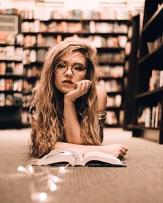 a woman laying on the floor in front of a bookshelf with her hand under her chin