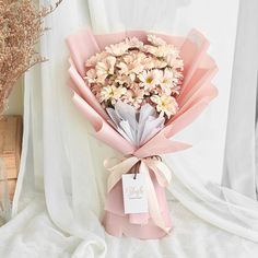 a bouquet of daisies wrapped in pink paper and tied to a ribbon with a name tag