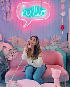 a woman sitting on a pink couch in front of a neon sign that says hello