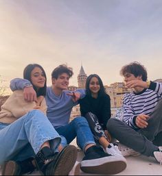 four young people are sitting on the ground and posing for a photo with buildings in the background