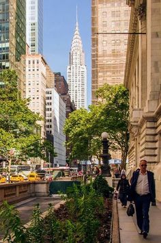 a man walking down a sidewalk next to tall buildings in a city with lots of trees