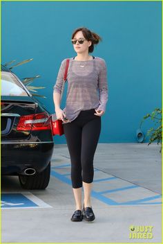 a woman in black leggings and a gray shirt is walking past a car