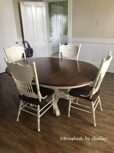 a dining room table with white chairs and a brown wooden table in front of a doorway