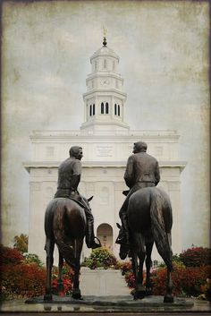 two statues of men riding horses in front of a white building with a steeple