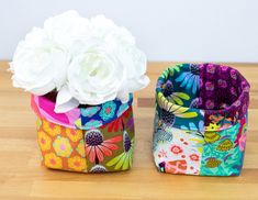 two colorful flower pots sitting on top of a wooden table next to each other with white flowers in them