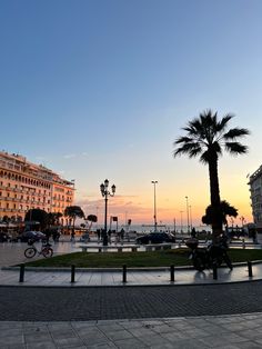 a person riding a bike down a street next to tall buildings and palm trees at sunset