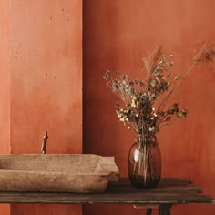 a vase filled with flowers sitting on top of a wooden table next to a wall