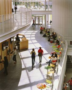 people are walking around in the lobby of a large building with many tables and chairs