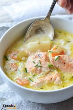 a bowl of soup with salmon, potatoes and carrots is being spooned into it