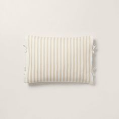 a white and beige striped pillow with tassels on the bottom, sitting on a white surface