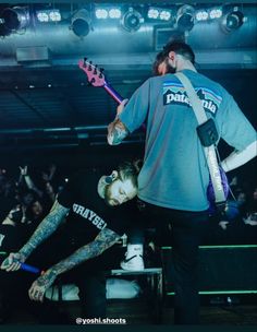 two men with tattoos on their arms are playing guitar in front of an audience at a concert