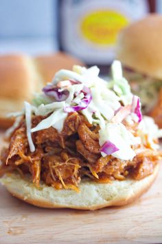 a pulled pork sandwich with coleslaw slaw on it and two rolls in the background