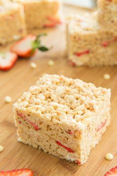 some rice krispy treats sitting on top of a cutting board next to sliced strawberries