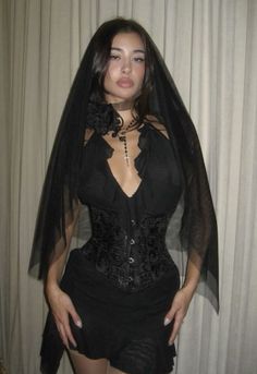 a woman in a black corset and veil posing for the camera with her hands on her hips