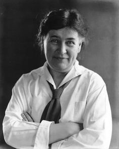 an old black and white photo of a woman wearing a shirt and tie with her arms crossed