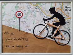 a paper cut out of a man riding a bike on top of a hill next to a road sign