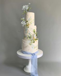 a three tiered wedding cake with blue ribbons and flowers on the top, sitting on a pedestal