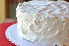 a white frosted cake sitting on top of a red and white tablecloth covered plate