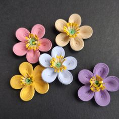 four different colored paper flowers on a black surface with one flower in the center and two are yellow, white, and purple