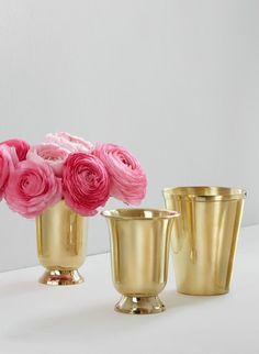 three gold vases filled with pink flowers on top of a white table next to each other