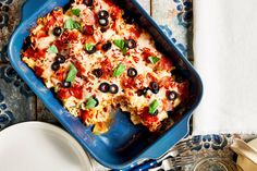 a blue casserole dish with olives and cheese on it next to silverware