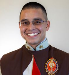 a man wearing glasses and a uniform smiling at the camera while standing in front of a white wall