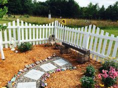 a white picket fence surrounding a garden with flowers and stones on the ground in front of it