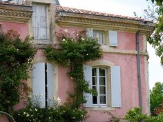 an old pink house with white shutters and flowers growing on the side of it