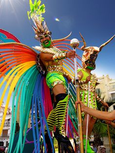 two women in colorful costumes and headdresses dancing with each other on the street