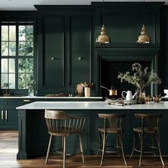 a kitchen with dark green cabinets and white counter tops, gold pendant lights over the island