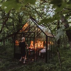 a woman standing in front of a small glass house surrounded by trees and greenery