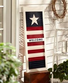 an american flag welcome sign sitting on the side of a house with potted plants next to it