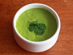 a white bowl filled with green soup on top of a wooden table