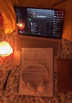 an open laptop computer sitting on top of a bed next to a book and candle