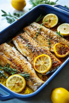 baked fish with lemons and herbs in a blue casserole dish