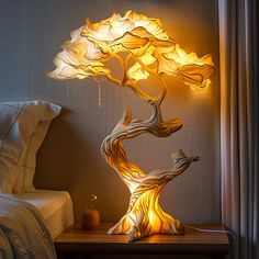 a lamp that looks like a tree with leaves on it is lit up next to a bed