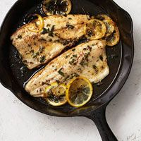 chicken with lemons and herbs in a skillet on a white counter top, ready to be cooked