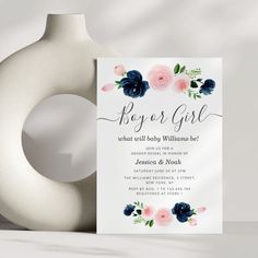 a white vase sitting next to a blue and pink flowered baby shower party card