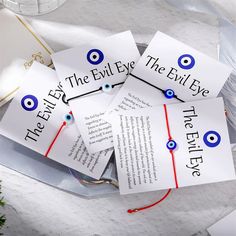 four evil eye cards with red string and blue eyes on them sitting on a table