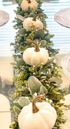 a long table with white pumpkins and greenery on the top, in front of a window