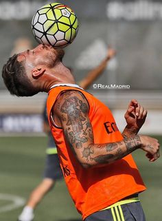 a man in an orange shirt is reaching up to catch a soccer ball with his head